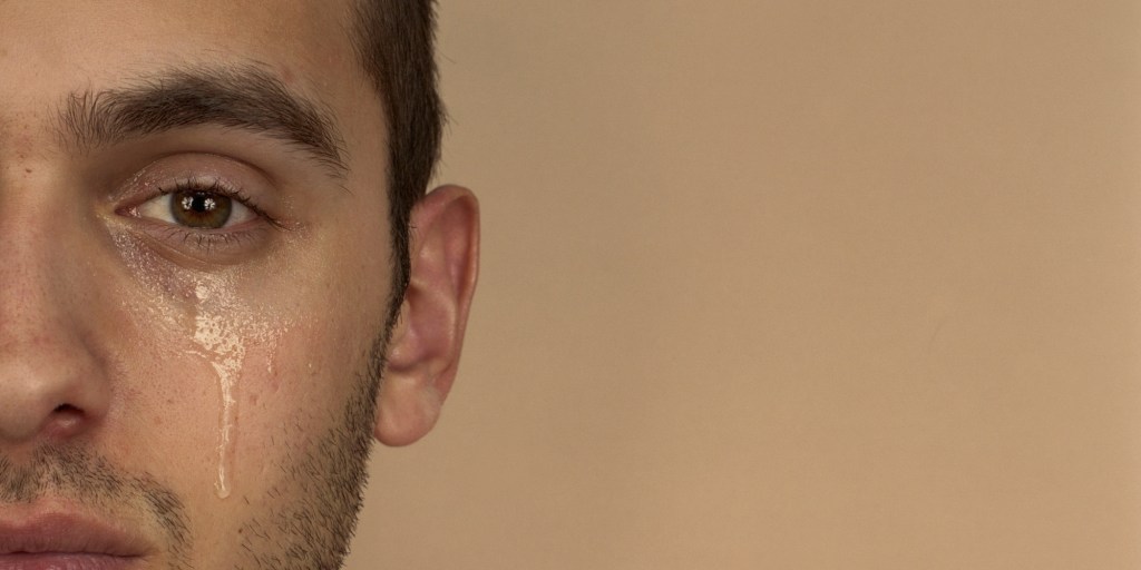 Young man with tear rolling down cheek, portrait, close-up
