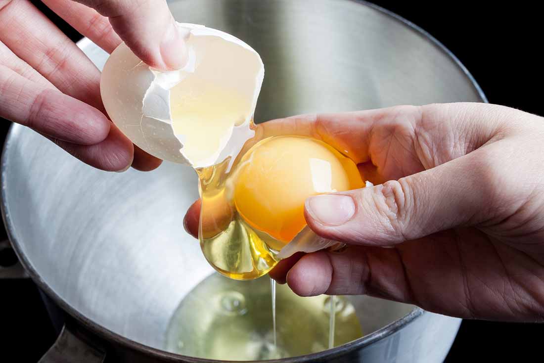 Separating yolk and white of the egg above metal bowl